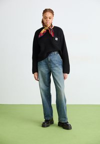 Črno rebrasto pleteno pulover s žepom na prsih, modri jeans z zbledelim videzom in črne platform škornje. Barvit vzorčast šal okoli vratu.