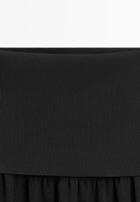 Gros plan d’un vêtement noir montrant une large ceinture côtelée au-dessus d’un tissu froncé en dessous.