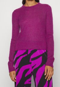 Fuchsia stickad tröja med långa ärmar och rund halsringning, med en mjuk textur och ribbat avslut. Kombinerad med mönstrade byxor.