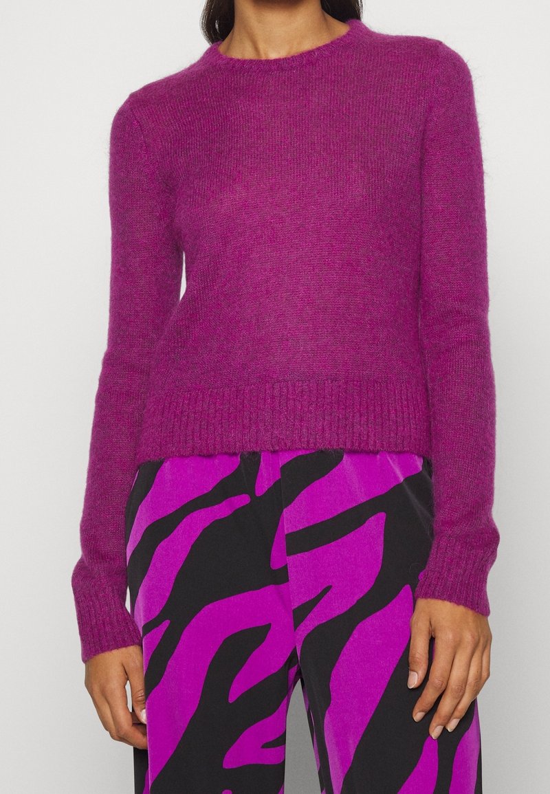 Fuchsia stickad tröja med långa ärmar och rund halsringning, med en mjuk textur och ribbat avslut. Kombinerad med mönstrade byxor.