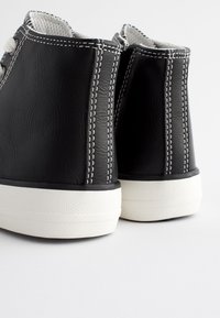 Baskets montantes en cuir noir avec coutures blanches et semelles en caoutchouc, dotées d'une finition texturée et d'accents blancs contrastants.