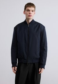 Μπλε ναυτική μπουφάν βομβαρδιστικού με εμπρόσθιο φερμουάρ, ριμπ μανσέτες και υφή υφάσματος, με άνετη εφαρμογή και μινιμαλιστικό σχεδιασ μό.