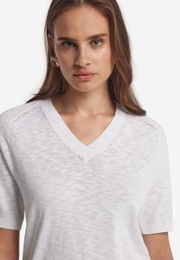 Vit V-ringad tröja med korta ärmar, lätt textur och subtilt mönster. Urringningen har en ribbad kant. Mjuk och avslappnad design.