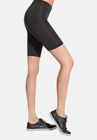 Czarne elastyczne krótkie spodenki kolarskie z wysokim stanem, gładką fakturą i przylegającym krojem, zestawione z niskimi czarnymi trampkami z białymi podeszwami.