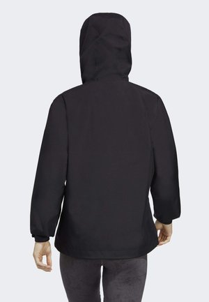 Persoon draagt een zwarte capuchonjas met lange mouwen en elastische manchetten, kijkend weg, tegen een effen lichte achtergrond.