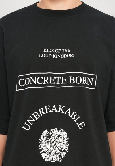 Svart T-skjorte med hvit tekst: "KIDS OF THE LOUD KINGDOM," "CONCRETE BORN" i en boks, "UNBREAKABLE" buet over et ørnerelief.