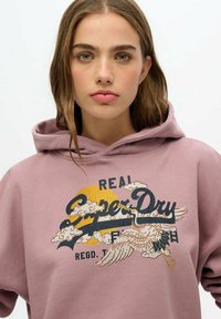 Pink hoodie with a front graphic featuring a yellow sun, clouds, and bird design in rhinestones. Soft texture and relaxed fit.