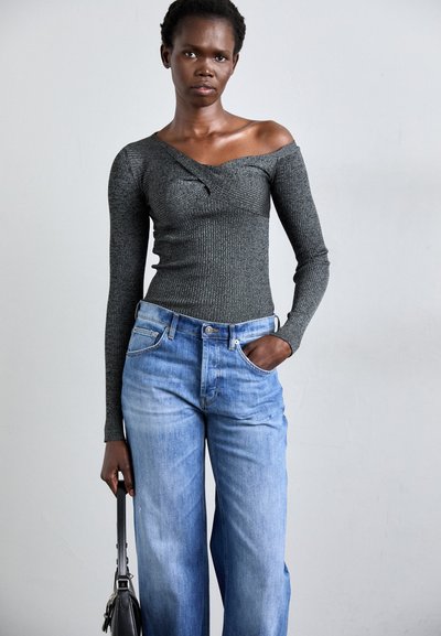 Dark gray ribbed long-sleeve top with an off-shoulder design, paired with light blue wide-leg jeans. Model holds a small black handbag.