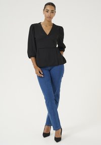 Černý peplum top s véčkovým výstřihem a balónovými rukávy, doplněný o modré úzké džíny a černé vysoké podpatky. Hladká textura, jednobarevný.