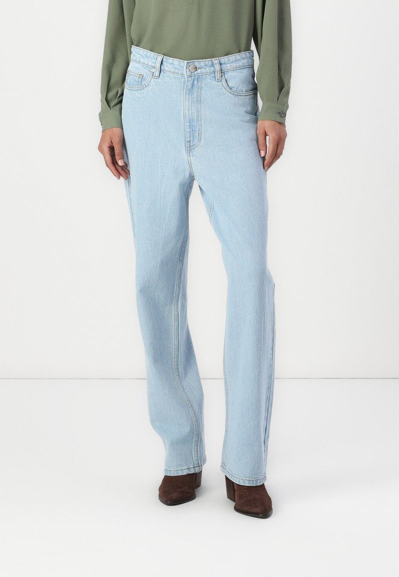 Lyseblå denimjeans med høy midje, rett ben-design og frontlommer, parret med mørkebrune hælankelstøvler.