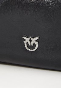 Zwarte leren handtas met textuur, voorzien van een zilveren metalen ring versierd met twee tegenover elkaar staande vogels als decoratieve accent.