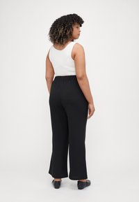 Black wide-leg pants with an elastic waistband, paired with a white tank top. The fabric appears soft with a smooth texture.