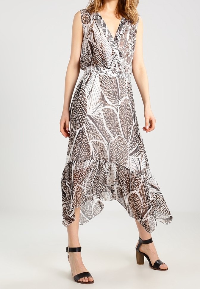 Flödande klänning med ett lövtryck i brunt och vitt, med v-ringning, ärmlöst design och asymmetrisk fåll. Stylad med svarta sandaler.
