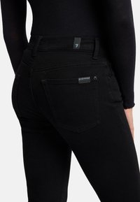 Svarte denim jeans med en tettsittende design, baklommer med subtil merkevare og en glatt, teksturert overflate.