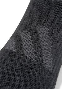 Schwarze Socke mit gerippter Textur. Besitzt ein dezentes Logo-Muster in einem helleren Grauton. Die Zusammensetzung deutet auf einen Materialmix für zusätzlichen Komfort hin.