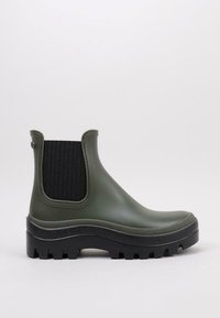 Botín de goma verde hasta el tobillo con un panel lateral elástico negro, suela con agarre texturizado y punta redonda. Presenta un acabado suave y un hardware mínimo.