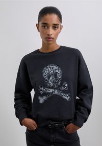 Sudadera negra con un gráfico de calavera y huesos cruzados con detalle texturizado. El diseño incorpora varios patrones con un acabado brillante.