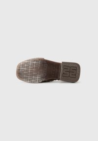 Brown leather shoe sole with a textured pattern and block heel. Markings include brand logo and style details embossed on the side.