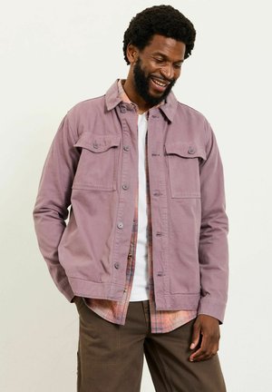 Purple cotton jacket with two chest pockets, button closure, and a rounded collar, layered over a checked, multi-colored shirt.