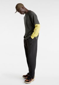 Maglietta grigia con maniche lunghe gialle, pantaloni neri e scarpe da ginnastica multicolori. Caratterizzata da un logo sul petto e sulla manica. Tessuto texturizzato.