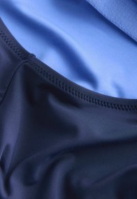 Mereväe sinist ujumisriide kangast, mis on sileda ja läikiva tekstuuriga. Sellel on õmmeldud serv ja kontrastne heledam sinine vooder.