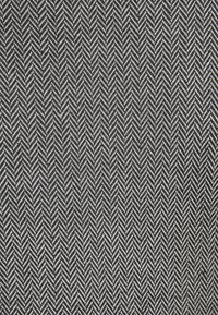 Černobílá kostkovaná textilie s vzorem ve tvaru chevronu, která má texturovanou vazbu a ukazuje střídající se tmavé a světlé vlákna.
