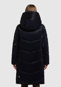 Must must coat kõrge kraega, nurgelise mustriga ja pikad varrukad. Sile, läikiv kangas koos küljetaskute ja brändi siltidega.