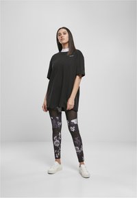 Svart oversized t-shirt med korta ärmar, kombinerad med svarta blommiga leggings med genomskinliga detaljer. Vita sneakers fulländar outfiten.