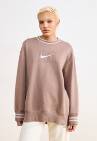 Sweatshirt marrone oversize con logo Nike e ricamo, caratterizzato da polsini a costine con due strisce e un collo rotondo. Texture morbida.