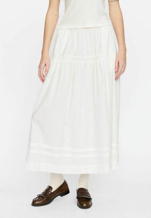 Jupe maxi en coton blanc avec taille froncée, deux rayures horizontales à l'ourlet, associée à des mocassins en cuir marron et des chaussettes crème.