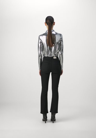 Chemise à manches longues en sequins argentés associée à un jean noir évasé et des bottes noires à talons aiguilles, vue de dos.
