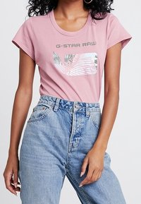 Světle růžové bavlněné tričko se stylovým potiskem s palmami a textem "G-STAR RAW". V páru s vysokým modrým džíny.