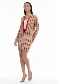 Ținută din tricot care include un cardigan cu dungi și o fustă asortată în nuanțe de bej, roșu și alb. Cardiganul are un design scurt și este deschis pe față.