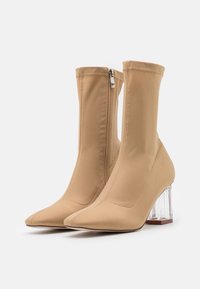 Beiget nilkkurit, joissa on istuva muotoilu ja sileä kangas. Varustettu terävällä kärjellä ja kirkkaalla paksulla korolla, sivussa vetoketjusuljenta.