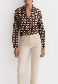 Camisa de botones en patrón geométrico negro y crema, de manga larga, combinada con pantalones beige ajustados, de textura suave y corte relajado.