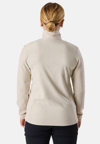 Haut beige à manches longues avec un col haut, fabriqué en tissu doux. Présente une coupe ajustée et une texture lisse, sans motifs ni éléments métalliques visibles.