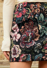 Čierna kvetinová mini sukňa s výraznými, textúrovanými vzormi v červenej, ružovej a zelenej farbe. Mäkká látka s komplikovanými švami.