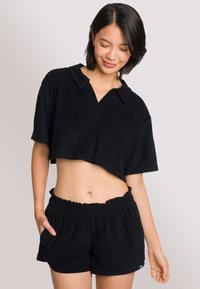 Polo top corto nero con maniche corte, realizzato in tessuto morbido. Abbinato a pantaloni corti neri con vita arricciata, dotati di una cintura elastica.