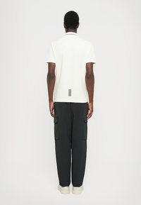 Witte polo met zwarte kraag, met horizontale strepen op de achterkant. Gecombineerd met zwarte cargo broek en witte sneakers.