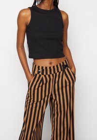 Svart kortärmad tanktopp med rund halsringning, tillsammans med högmidjade bruna och svarta randiga vida byxor med sidofickor och knappar.