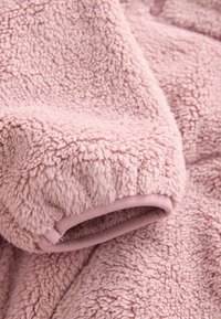 Helles rosa Fleece-Gewebe mit einer plüschigen, strukturierten Oberfläche und glatten Bündchendetails. Das Material ist weich und hat ein gemütliches Aussehen.