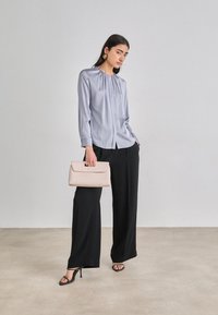 Vaaleanharmaa paita, jossa on pleatattu kaula-aukko, mustat leveälahkeiset housut, mustat remmikengät ja vaaleanpunainen clutch-käsilaukku. Sileät pinnat.