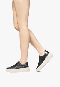 Czarne skórzane sneakersy z masywną białą podeszwą, z sznurowanym zapięciem, gładką fakturą i subtelnymi akcentami po bokach.