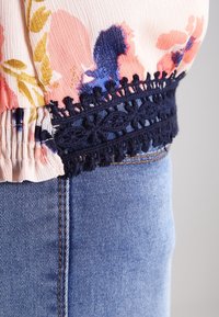 Hedvábný top s květinovým vzorem a naškrobeným pasem, doplněný námořnickou krajkou. V kombinaci se světle modrým džínsovým materiálem, který má v�ýrazné švy.