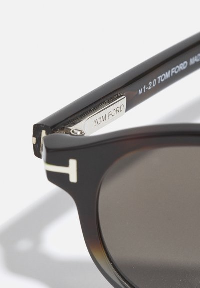 Schwarz- und schildpattfarbene Sonnenbrille mit dunklen Gläsern. Sie verfügt über ein silbernes, graviertes Logo am Bügel und ein sauberes, modernes Design.