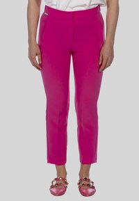Strakke roze broeken met een gladde textuur, zijzakken en een slank ontwerp, gecombineerd met roze schoenen met gouden accenten.