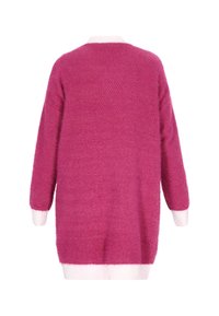 Pitkähiha sweater kirkkaan vaaleanpunaisena, jossa on tekstuuri neulontana. Ominaisuuksiin kuuluvat valkoiset ribbineulekaulus ja helma. Takakatsaus osoittaa suurikokoisen istuvuuden.