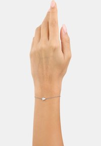 Pulsera de cadena de plata con una pequeña gema clara, llevada en la muñeca. Tono de piel visible, mano levantada en una posición relajada.