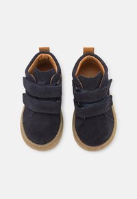 Zapatos de ante azul marino con dos correas de Velcro, suelas de goma marrón claro y forro interior beige, con punteras redondeadas y una lengüeta.