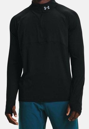 Czarna sportowa bluza z długim rękawem, zamkiem do ćwiartki i logo Under Armour na kołnierzu, noszona z niebieskimi spodniami, ręce widoczne po bokach.